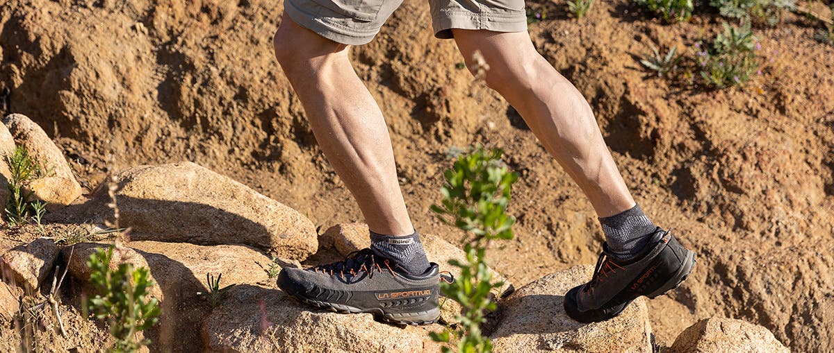 A man hiking on dirt and rocks wearing Injinji Outdoor Midweight Mini-Crew Wool performance socks. 