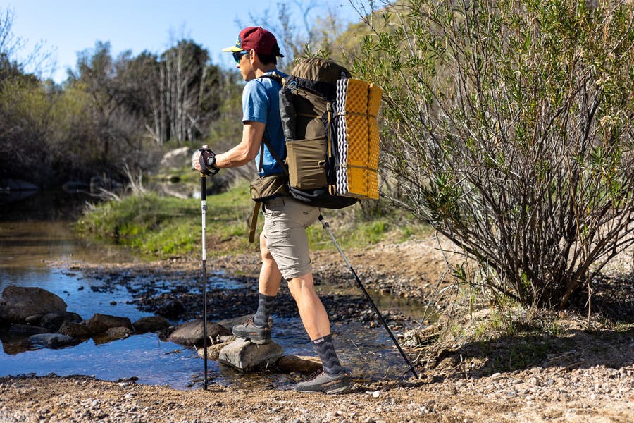 Hiker crossing a creek wearing the Outdoor Midweight Crew in slate Merino Wool. 