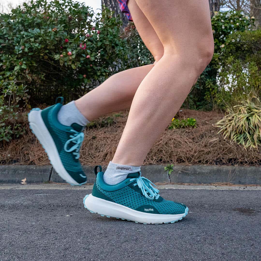 A person running on a concrete path wearing Injinji Run Lightweight Mini-Crew socks in gray.