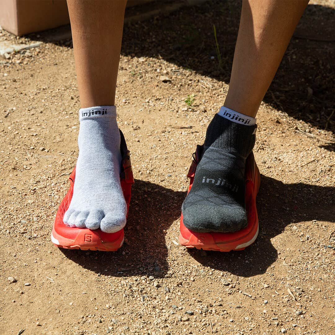 A person's feet wearing Injinji Liner + Runner socks resting on top of trail running shoes.