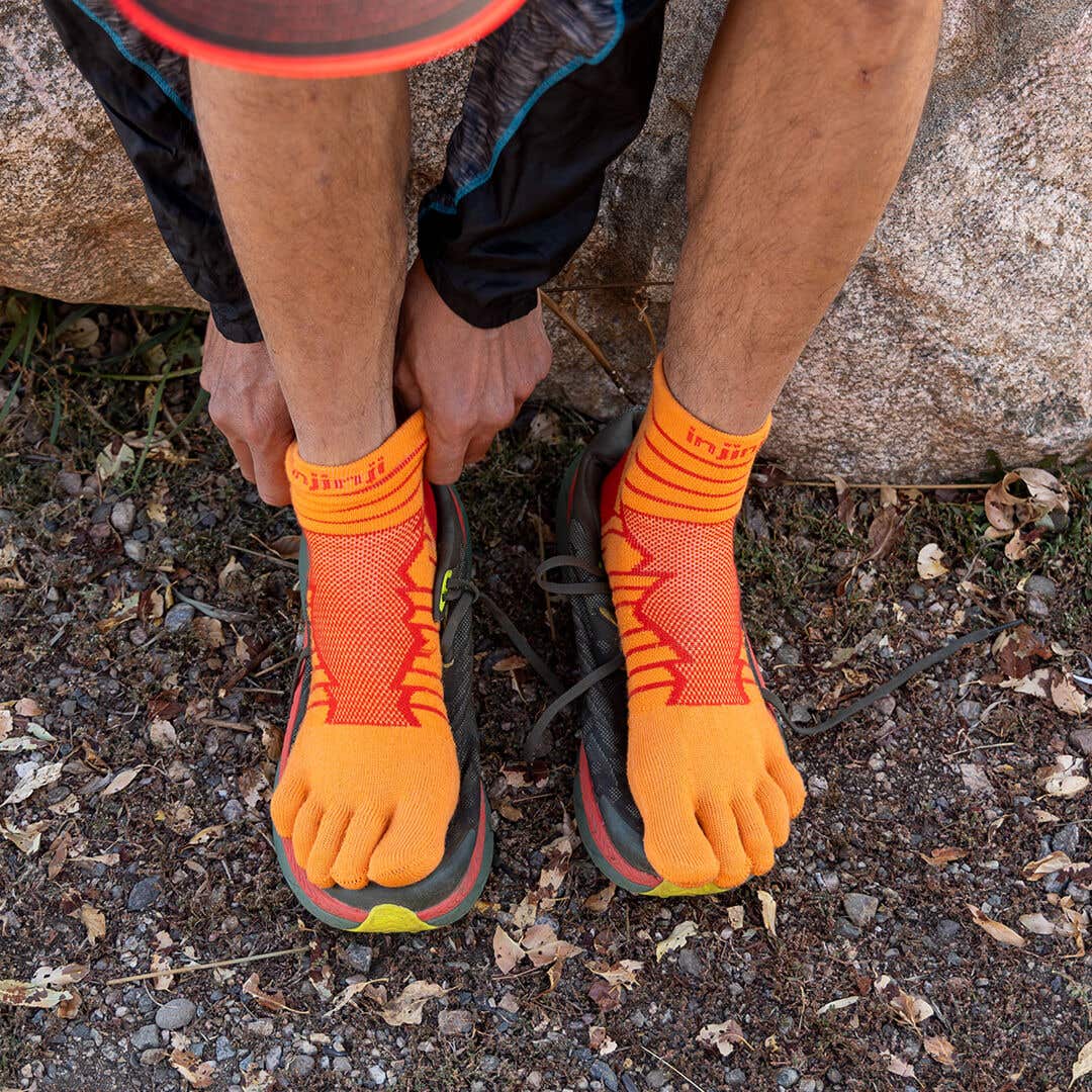 A person bent over their legs adjusting their Injinji Ultra Run Mini-Crew sock in Desert Orange.