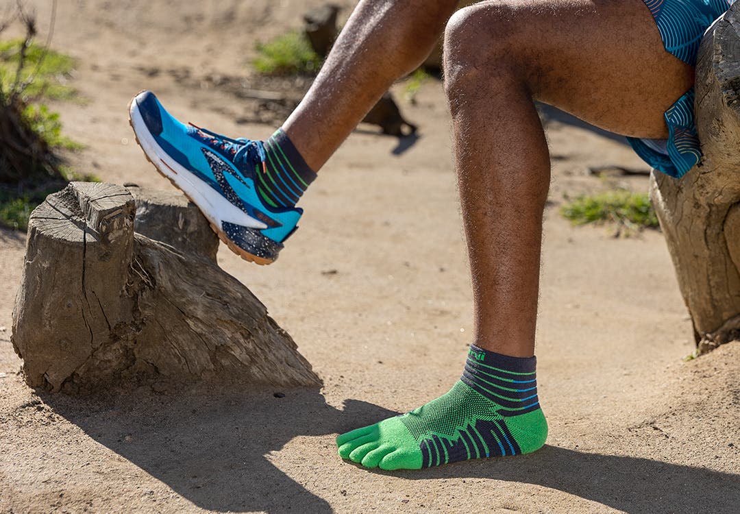 A runner resting on a dirt trail wearing Injinji Ultra Run Mini-Crew performance toesock in an online exclusive color called Emerald.