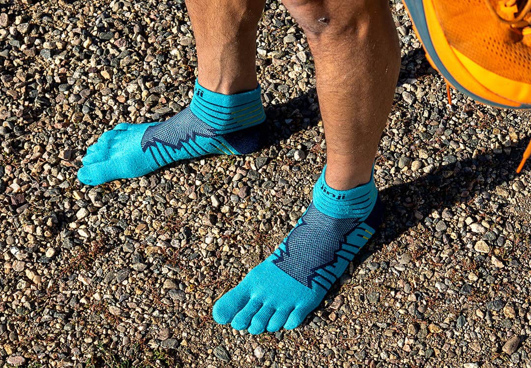 A runner standing on a packed gravel travel wearing Injinji Ultra Run Mini-Crew socks in Pacific Blue.