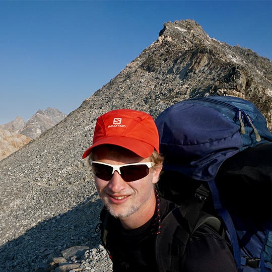 Male backpacker near a rocky peak through the Sierra Nevada mountain range in California. 