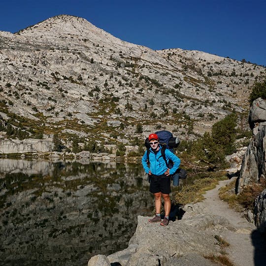 Male backpacker standing next to a lake with the reflection of the mountains on the water. Male backpacker standing next to a lake with the reflection of the mountains on the water.